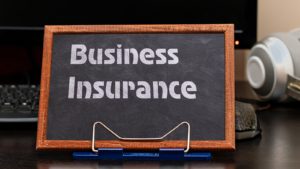 Business Insurance Services Concept. The text is written on a chalk board located at the workplace near the computer.